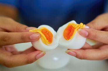 A close-up view of two hands gently splitting a soft-boiled egg, revealing its golden, runny yolk. The image showcases the delicate texture of the egg, with the creamy yolk oozing out against the smooth, cooked egg white.