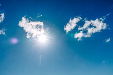 Bright sun shining through fluffy white clouds in deep blue sky