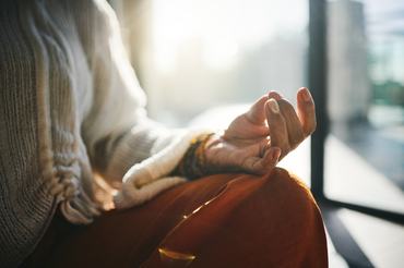 A close-up of a person meditating, wearing neutral-toned clothing, bathed in soft morning sunlight. The hand in a mudra gesture conveys calm and mindfulness.